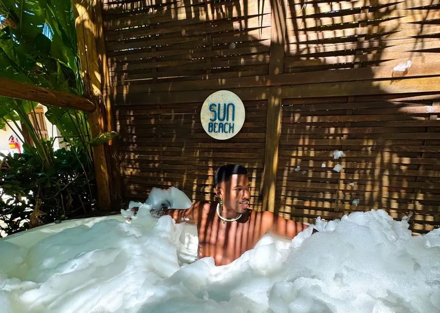 Cliente relaxando na jacuzzi com espuma, ao lado da placa da Sun Beach