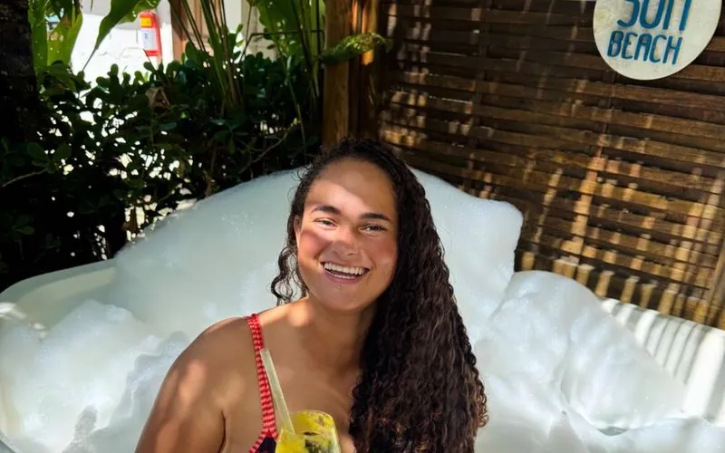 Cliente sorrindo com um drink dentro da jacuzzi com espuma